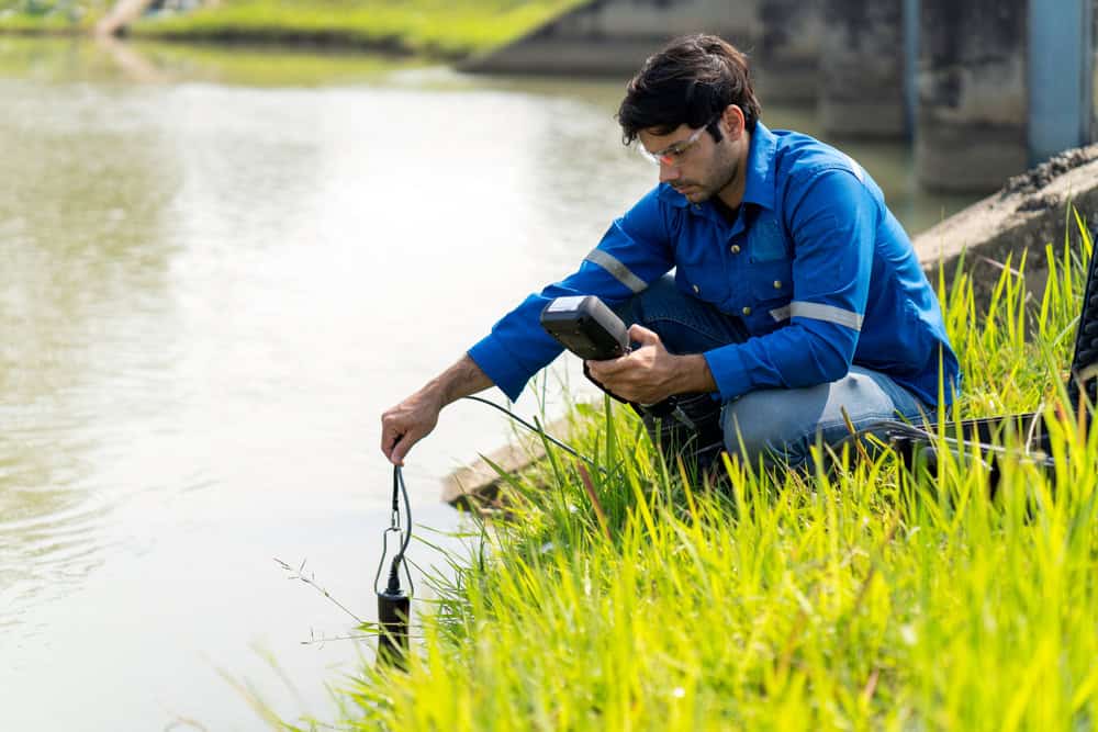 Person kneeling beside water canal taking a reading.