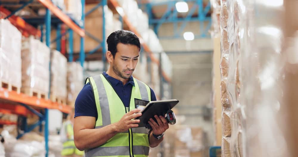 Warehouse worker standing in a warehouse looking at an iPad.